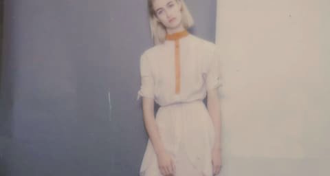 Woman in a pale dress in front of a grey wall, softly blurred