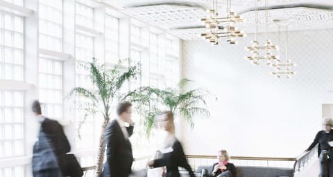 Fondsmesse Schweiz: blurred visitors walking past a palm in a hall with tall windows
