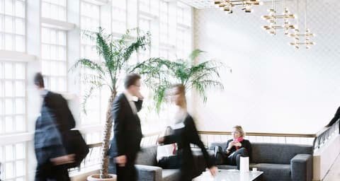 Visitors in motion blur in a bright hall with palm and chandeliers at Fondsmesse Schweiz