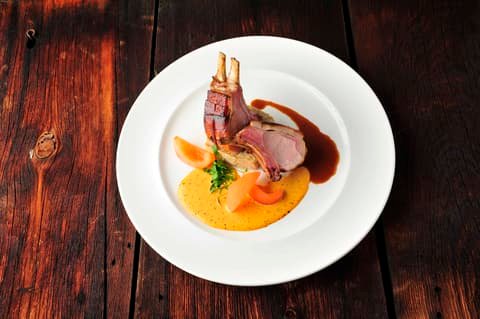 Rack of lamb with sauce and vegetable purée on a white plate, cooked by Klaus Leuenberger