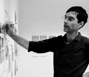 Roman Imhof drawing on a wall covered with sketches, black-and-white portrait