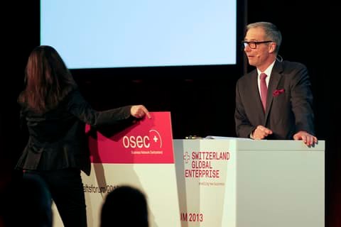 On stage, the old Osec sign is removed from a lectern bearing the new Switzerland Global Enterprise logo