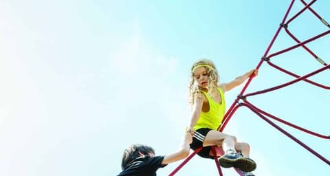 Two children on a red rope climbing frame against a blue sky, Swiss Medi Kids