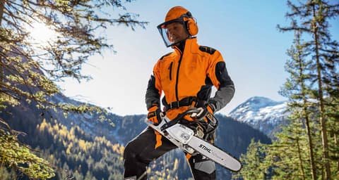 Forestry worker in orange protective gear holding a Stihl chainsaw in a mountain forest