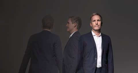Sacha Willemsen in a dark suit, shown three times: from behind, in profile and facing the camera