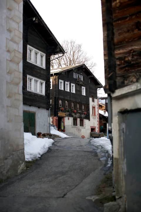 Village lane with dark timber houses and patches of snow near the restaurant St. Georg