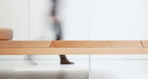 Blurred figure walking past a long wooden bench from Roger Stüssi's furniture collection