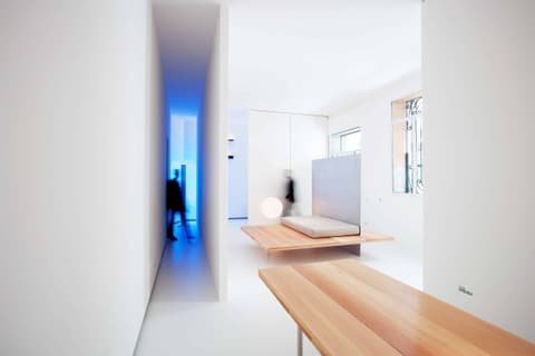 Roger Stüssi showroom: white room with wooden bench, daybed and a blue-lit corridor